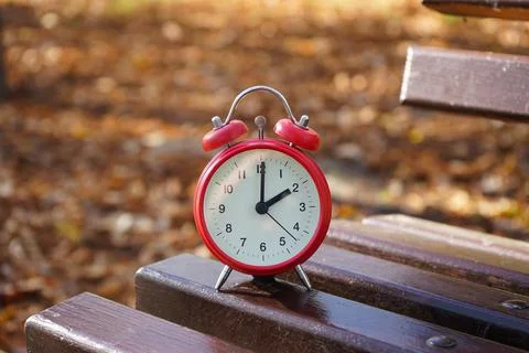 The concept change time. Alarm clock on a wooden bench in the autumn park. Foto stock