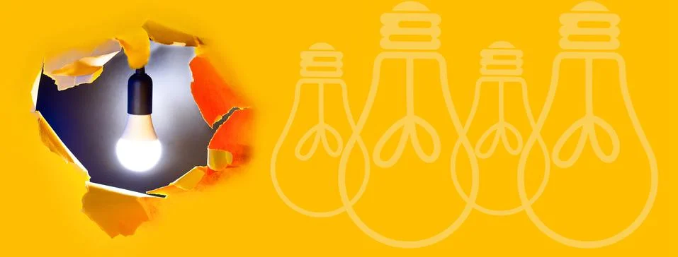 Concept of creative idea. A light bulb shines in hole of yellow paper Stockfoto's