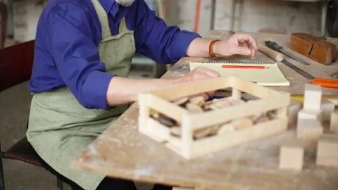 Concept of diy. Old man is making a sketch of birds house from wood. Stock Footage 91044915