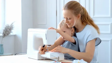 Concept during self-isolation and quarantine. A woman with a small child sews a Stock Footage 127740496
