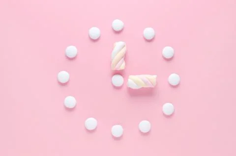 Concept image, a clock with candy and marshmallow in pastel colors on pink Stock Photos