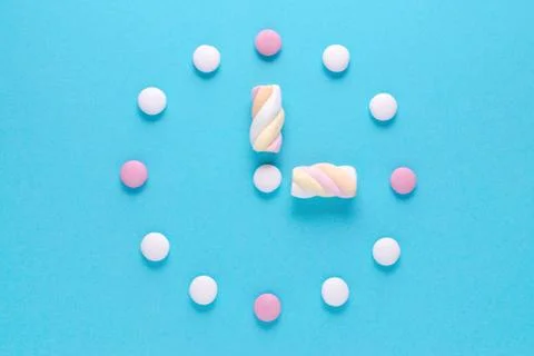 Concept image, a clock with candy and marshmallow on blue background Stock Photos