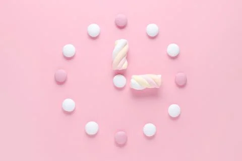 Concept image, a clock with candy and marshmallow, pastel colors on pink Stock Photos