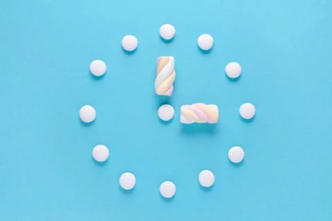 Concept image, a clock with candy and marshmallow on blue background, flat lay Stock Photos