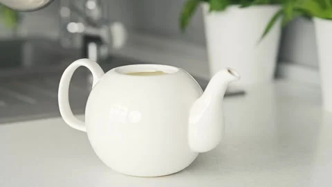 Concept of making tea. Boiling water pours into white ceramic teapot on the Видео 220555599