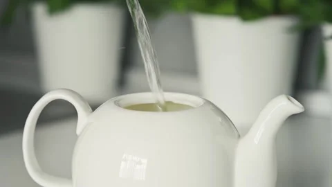 Concept of making tea. Boiling water pours into white ceramic teapot on the Видео 220555726