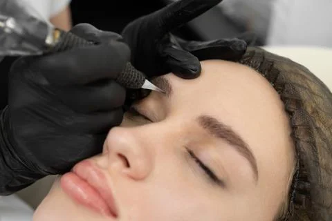 Concept of microblading eyebrows. The cosmetologist performs the procedure of Stock Photos