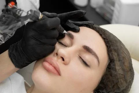Concept of microblading eyebrows. The cosmetologist performs the procedure of Stock Photos