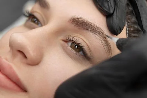Concept of microblading eyebrows. The cosmetologist performs the procedure of Stock Photos