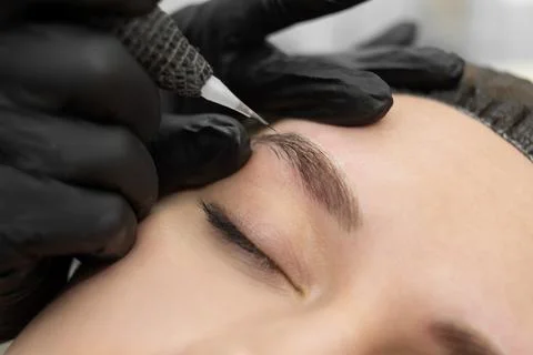 Concept of microblading eyebrows. The cosmetologist performs the procedure of Stock Photos