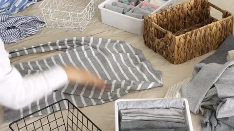 The concept of organizing and storing clothes. A woman folds a sweater and a T Stock Footage 236966024