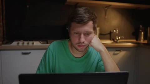 Concept of overworking at work. A tired man at a laptop sitting in the kitchen Stock Footage 244215006
