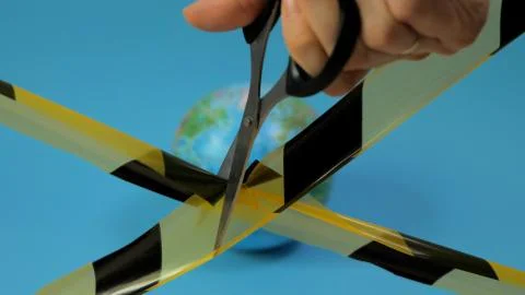 Concept: quarantine end. A hand with scissors cuts a black-yellow ribbon. Stock Photos