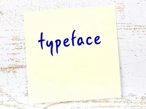 Concept of reminder about typeface. Yellow sticky sheet of paper on wooden wa Stock Photos