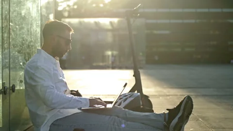 Concept of remote work. A middle-aged man in headphones sits on the sidewalk in Stock Footage 203707695