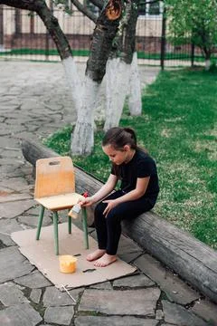 The concept of reusing old things, a child repaints an old chair with yellow  Stock Photos