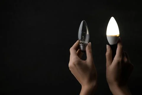 The concept of saving electricity. Light bulbs in hands on a black background Stock Photos