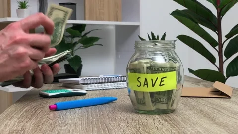 Concept of savings, a man puts 100 dollar bills in a glass jar Stock Footage 130356465