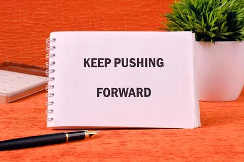 Concept text KEEP PUSHING FORWARD on a spiral notebook on an orange backgroun Stock Photos