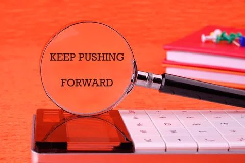 Concept text KEEP PUSHING FORWARD focused through a magnifying glass on an or Stock Photos