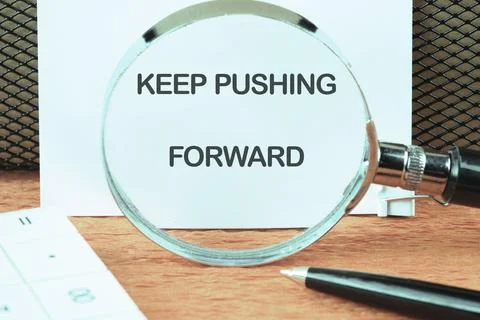 Concept text KEEP PUSHING FORWARD focused on the notebook through a magnify.. Stock Photos