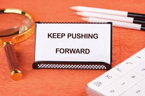 Concept text KEEP PUSHING FORWARD on the card next to a magnifying glass, pen Stock Photos