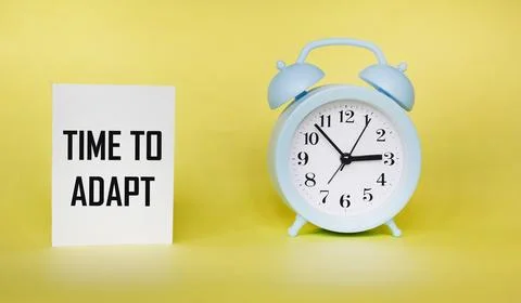 Concept Time to adapt on a notepad and a yellow background, next to a clock Stock Photos