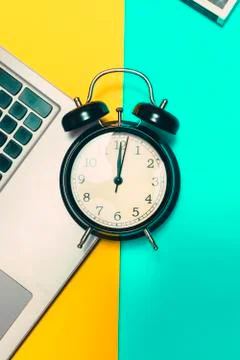 Concept time to work. Alarm clock with a laptop on a yellow and blue backgrou Stock Photos