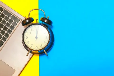 Concept time to work. Alarm clock with a laptop on a yellow and blue backgrou Stock Photos