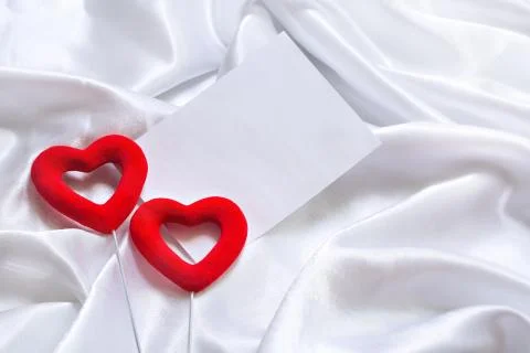 The concept of two lovers hearts lying on the white satin with white sheet of pa Stock-Fotos