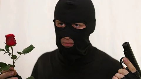 Concept war or peace. Young caucasian burglar with a pistol and a rose chooses a Stock Footage 112686917