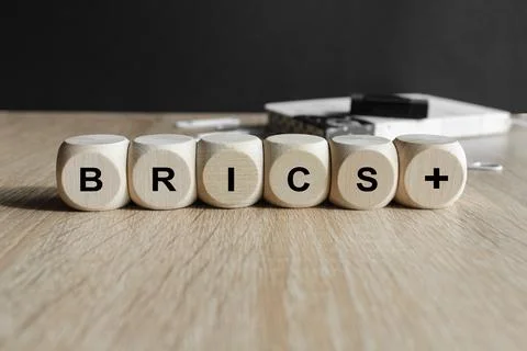 Concept word BRICS plus on cubes. Beautiful black background, wooden table. Stock Photos