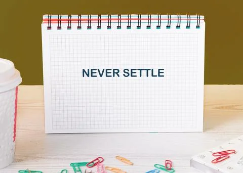 Concept words NEVER SETTLE in an open notebook surrounded by colorful paper c Stock Photos