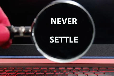 Concept words NEVER SETTLE through a magnifying glass on a laptop screen in a Stock Photos