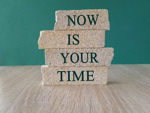 Concept words Now is Your Time on brick blocks. Beautiful green background Stock Photos