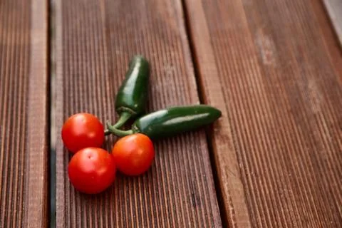 A conceptual composition of red cherry tomatoes and hot green chili peppers o Stock Photos