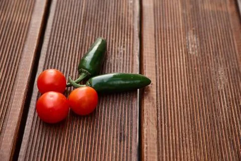 A conceptual composition of red cherry tomatoes and hot green chili peppers o Stock Photos