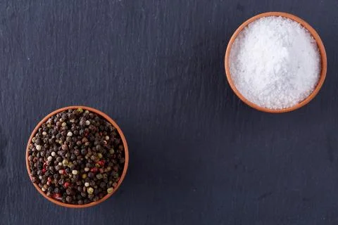 Conceptual composition of salt and pepper on spoons and bowls over dark Stock Photos