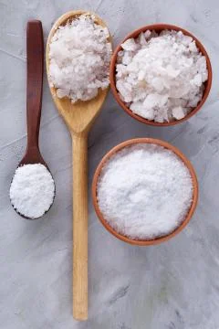 Conceptual composition of salt and pepper on spoons and bowls over light Stock Photos