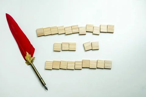 A conceptual flat lay featuring a red feather quill pen next to blank woode.. Stock Photos