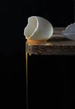 Conceptual image of a broken white eggshell with dripping egg yolk on black.. Stock Photos