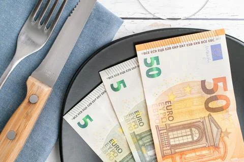 Conceptual studio shot of dinner table with euro bank notes on the plate instead Stock Photos