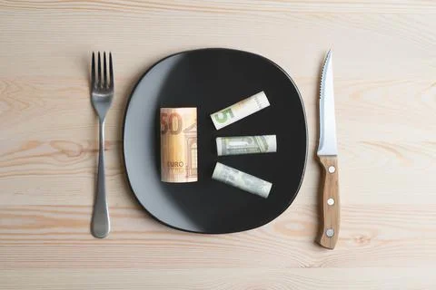 Conceptual studio shot of dinner table with euro bank notes on the plate instead Stock Photos