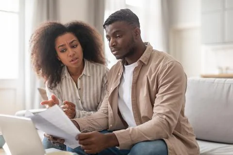 Concerned black married couple solving problems with papers at home Stock Photos
