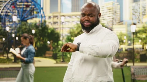 Concerned businessman checking time on smartwatch while standing in city park Stock Footage 343499652