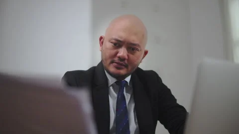 Concerned Businessman Working on a Laptop While Reviewing Documents Stock Footage 336870294