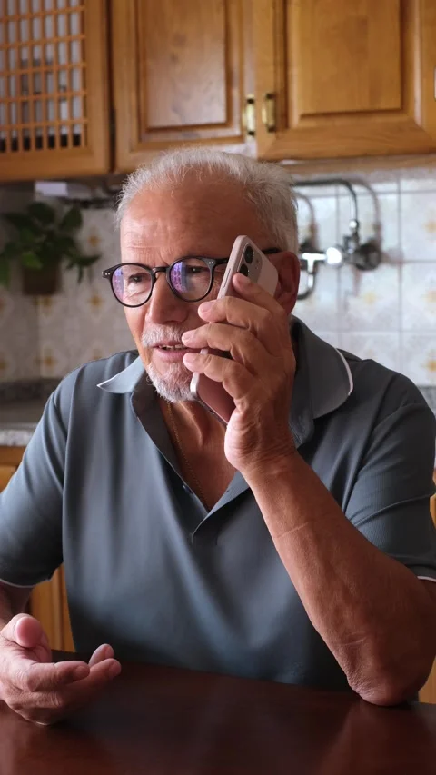 Concerned elderly man with eyeglasses speaking on his mobile phone at home Vídeos de archivo 344642763