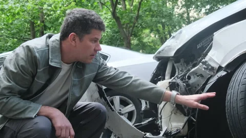 Concerned man squats down to inspect damaged automobile Stock Footage 281224710
