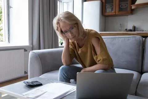Concerned mature worried homeowner woman checking bills for payment Stock Photos