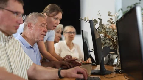 Concerned old man sitting at computer while trainer explaining him something Video stock 313457454